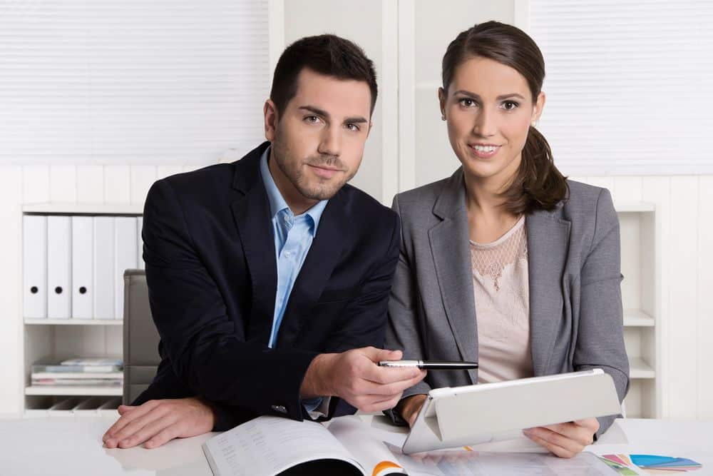 Two professionals in business attire working together with documents and a tablet.
